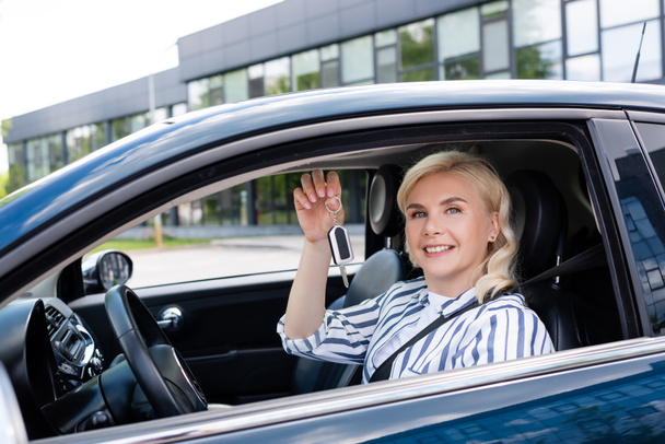 Happy blonde woman holding key on driver seat in car  - Foto, Imagen