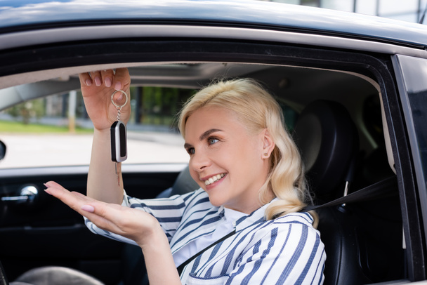 Blonde driver looking at key while sitting in auto  - Foto, Imagen