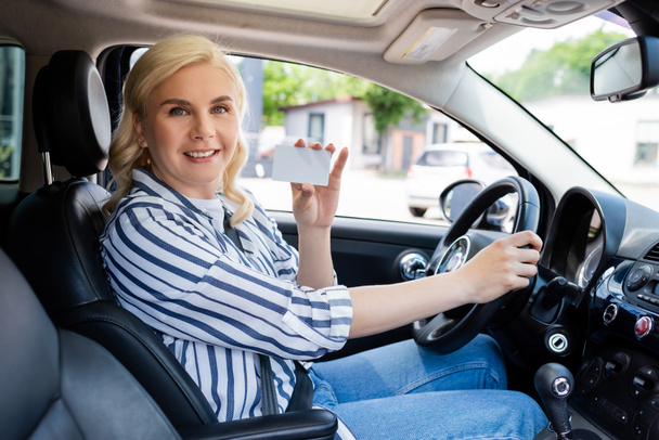 Positive blonde driver holding license in auto  - Zdjęcie, obraz