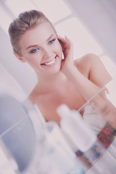 Young woman in bathrobe looking in bathroom mirror. - Foto, Imagen