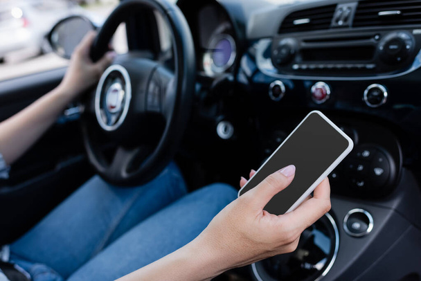 Cropped view of smartphone with blank screen in hand of driver in car  - Foto, imagen