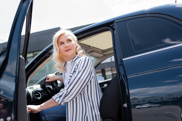 Блондинка дивиться далеко під час відкриття дверей авто на відкритому повітрі
  - Фото, зображення
