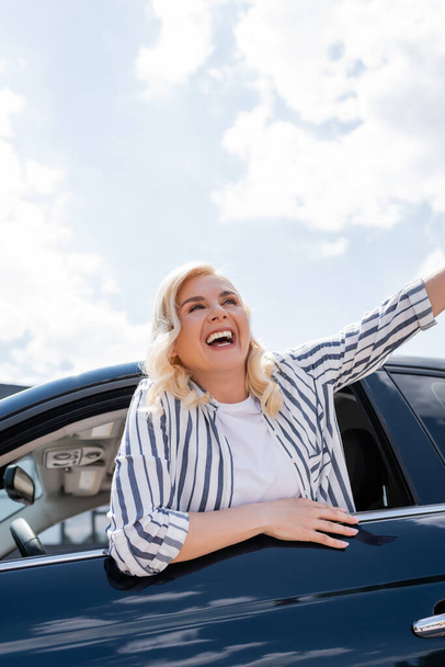 Cheerful blonde woman looking away from car window at daytime  - Foto, afbeelding