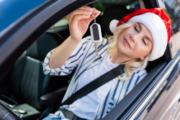 Blurred woman in santa hat holding key while sitting in car  - Foto, Imagen