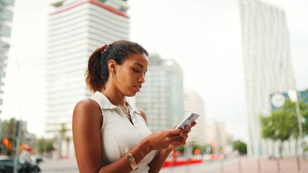 Clouse-up, cute tanned woman with ponytail wearing white top looking up at street signs and map trying to find her way using cellphone. Girl using map application outdoors - Fotó, kép