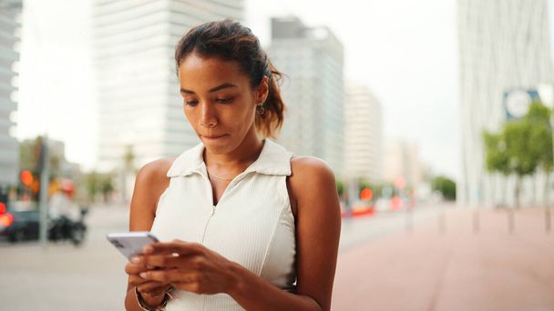 Clouse-up, cute tanned woman with ponytail wearing white top looking up at street signs and map trying to find her way using cellphone. Girl using map application outdoors - Foto, Bild