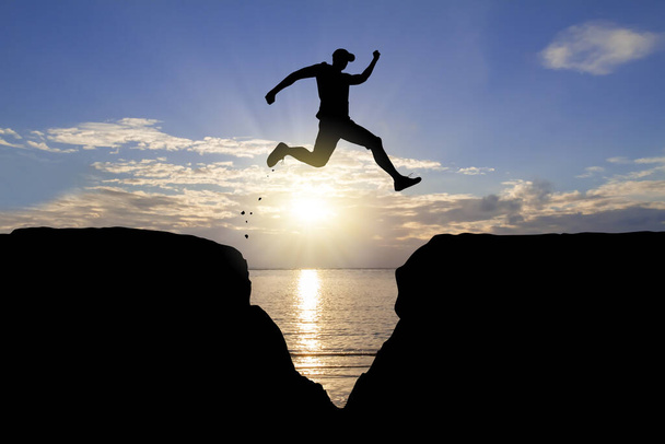 Silhouette of man jumping over the cliff on sunrise background, achievement business concept - Φωτογραφία, εικόνα