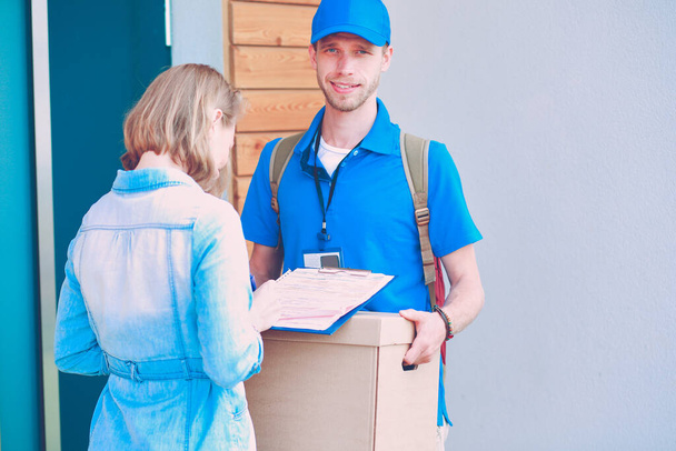 Smiling delivery man in blue uniform delivering parcel box to recipient - courier service concept. Smiling delivery man in blue uniform. - Фото, зображення