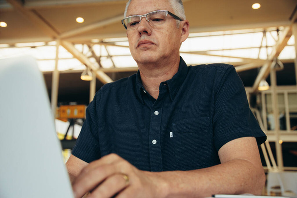 Serious caucasian mature male executive wearing eyeglasses doing research over laptop while working in corporate office - Valokuva, kuva
