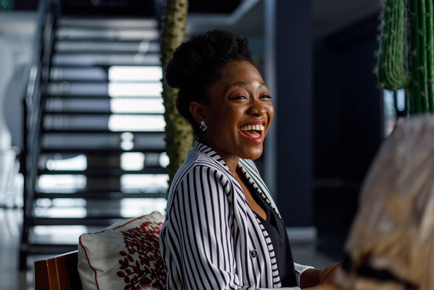 Χαρούμενη Αφροαμερικάνα νεαρή γυναίκα επαγγελματίας γελώντας και κοιτάζοντας μακριά, ενώ εργάζονται στο σύγχρονο εταιρικό γραφείο - Φωτογραφία, εικόνα