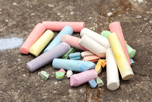 Heap of colorful pieces of drawing chalk laying on the ground, concrete floor, group of objects closeup, nobody, no people. Arts and crafts accessories and drawing tools concept outdoor art activities - 写真・画像