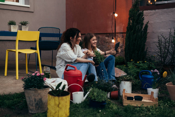 mother and daughter sitting on backyard porch, while gardening. daughter holding digital tablet - Fotografie, Obrázek