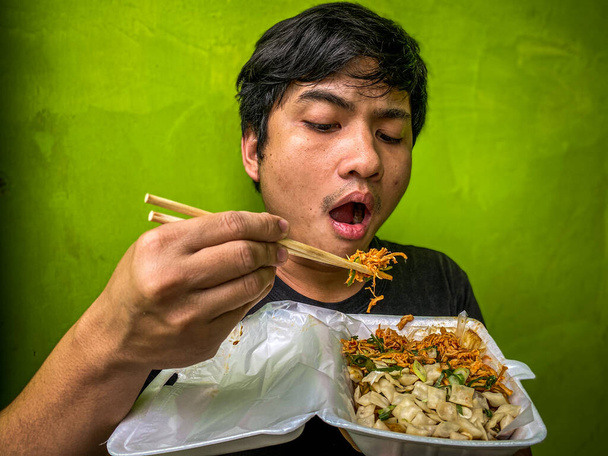 young hungry asian boy eats pangsit ayam manis or sweet chicken noodle dumplings on a plate. - Fotografie, Obrázek