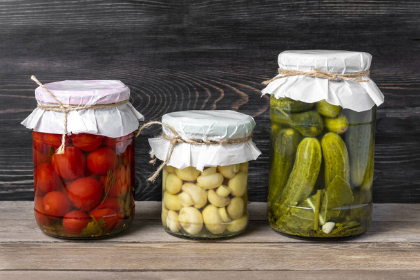 Homemade pickled cherry tomatoes, cucumbers, champignons, garlic, eggplant, red peppers in jars on wooden shelf Homemade canned and fermented foods concept Seasonal product. - Foto, Imagem