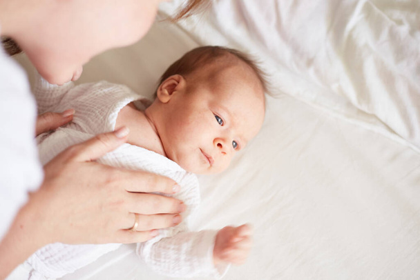 Mother dress her newborn baby boy. Realistic home portrait - Φωτογραφία, εικόνα