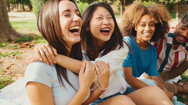 Happy multiethnic young people posing for the camera at picnic on summer day outdoors. Group of friends looking at the camera and laughing merrily - 写真・画像