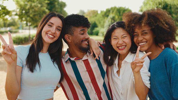 Happy, lovely multiethnic young people posing for the camera on summer day outdoors. group of friends hugging each other smiling at the camera while standing on path in the park - Foto, Imagem