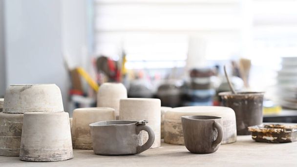 Handmade ceramic dishware set and pottery shaping tools on wooden table in creative studio. - 写真・画像