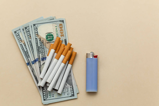 Cigarette and lighter on US dollars on a beige background. Conceptual photo about the dangers of smoking and the price of cigarettes. - Foto, Imagen