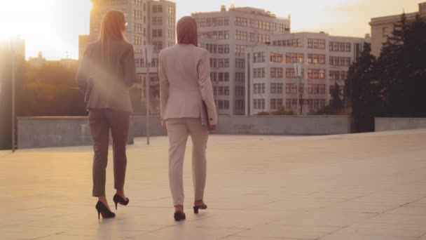 Kharkov, Ukraine 18.08.2021 Female colleagues entrepreneurs European woman in formal clothes and Indian girl in hijab walking stepping down street in sunset sunlight. Womens business fashion concept - 映像、動画