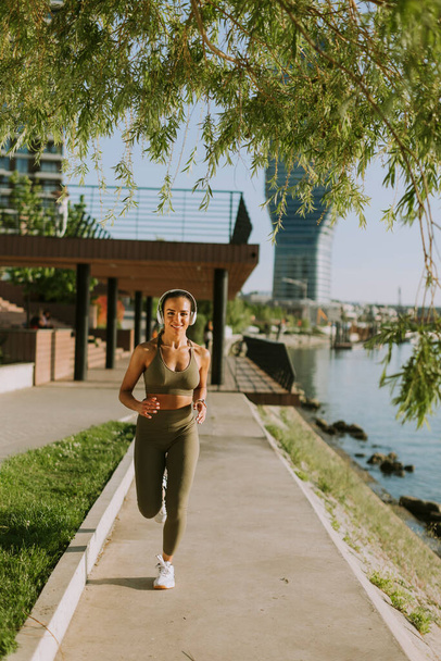 View at active young beautiful woman running on the promenade along the riverside - Foto, Imagen