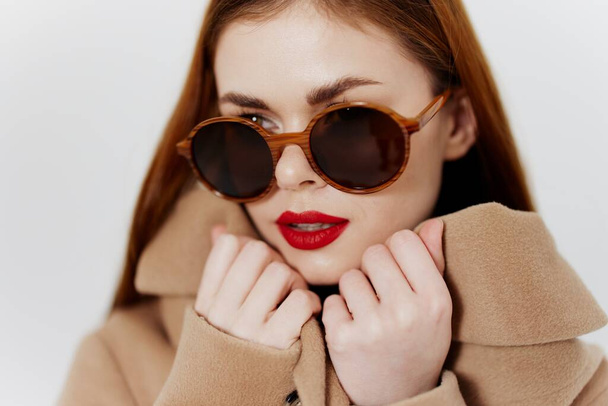 Palto mağazası için afiş. Gözlüklü genç kızıl saçlı bir kız stüdyoda beyaz bir arka planda ceket tasması tutuyor. Katalog fotoğrafçılığı. Yüksek kalite fotoğraf - Fotoğraf, Görsel