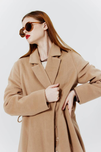 Fotografía del catálogo publicitario de la revista. Una chica de pelo rojo con estilo en un abrigo y gafas posa en el estudio sobre un fondo blanco. Foto de alta calidad - Foto, Imagen
