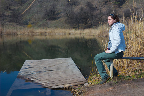 Caucasian woman sitting on a bench near the water. - Φωτογραφία, εικόνα