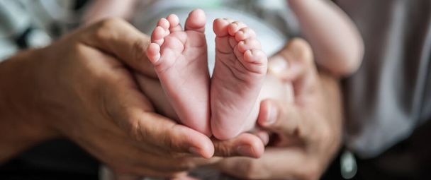 Close-up detail of parent holding cute and soft baby small leg in his hands. Macro abstract view of sweet baby foot fingers. Soft child skin feet. Love and family emotion - Photo, image