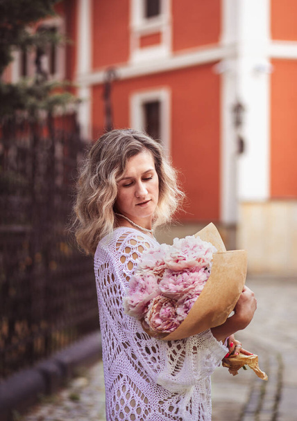 Positive girl hold flowers  in the city center. Close up shot of amazing blonde haired lady with natural make up look happy, walking outdoors  hold pink bouquet. - Foto, Imagen