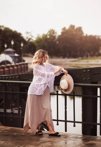 Beautiful blond young woman wearing  dress and straw hat enjoying sunrise on seafront in old european town. Fashion and style. Summer travel - Photo, Image