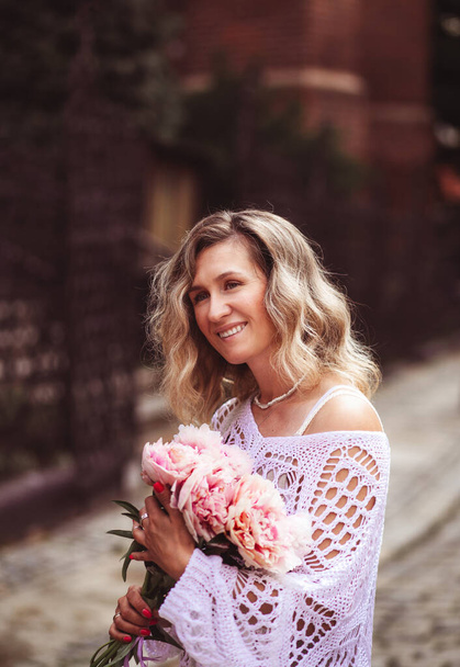 Positive girl hold flowers  in the city center. Close up shot of amazing blonde haired lady with natural make up look happy, walking outdoors  hold pink bouquet. - Foto, afbeelding