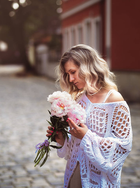 Positive girl hold flowers  in the city center. Close up shot of amazing blonde haired lady with natural make up look happy, walking outdoors  hold pink bouquet. - Photo, image