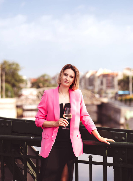 Young woman tourist standing with glass of white wine at bridge in european city , river at background  - Foto, imagen