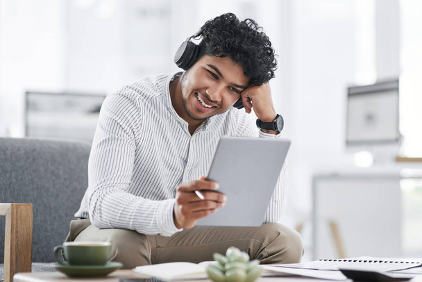 His connections allow him to achieve so much more. a young businessman wearing headphones while using a digital tablet in an office - Foto, Imagen