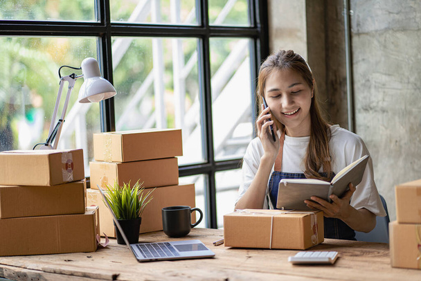 Small business startups, SME owners, Asian female entrepreneurs Work with boxes and laptops, smartphones. check order online To prepare to pack boxes to send parcels to sell to SME customers. Online business ideas. - Zdjęcie, obraz
