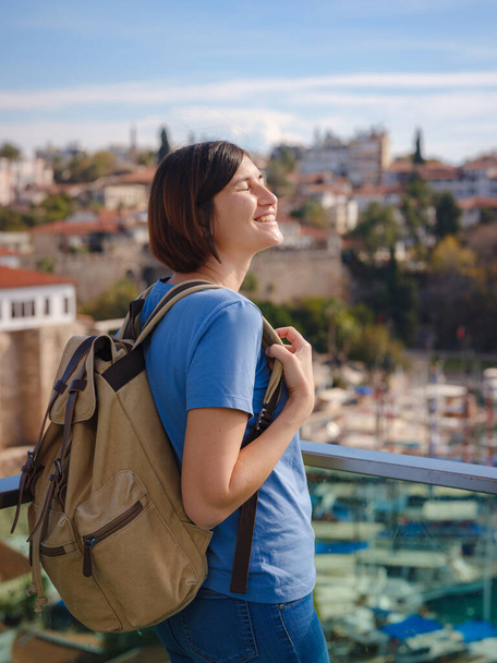 travel to Turkey, old town Antalya Kaleci. Happy asian female tourist traveller with backpack walks in old city. Woman on lookout over the old town and the port from viewpoint - Photo, Image