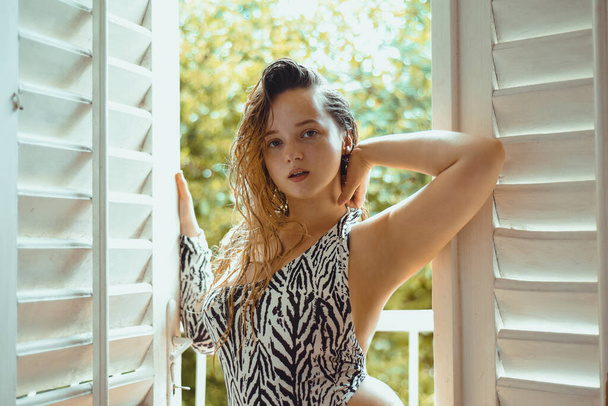 Gorgeous brunette portrait on the balcony in a swimsuit with an animal print zebra. Summer photo against the backdrop of sunset - 写真・画像