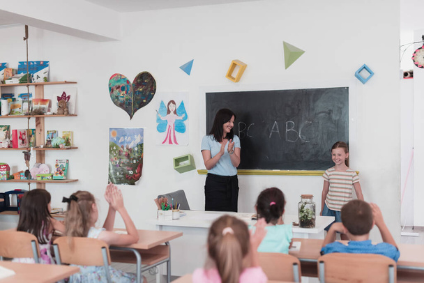 Elementary school. The female teacher helps the child student while writing the answer on the chalkboard. High quality photo - Photo, Image