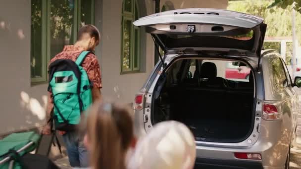 Family loading car trunk with field trip baggage while getting ready for summer holiday citybreak. Caucasian people putting voyage luggage and trolleys in vehicle while going on weekend vacation. - Séquence, vidéo