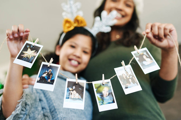 Decorate your home with happy family memories. a happy young mother and daughter hanging up family photographs during Christmas at home - Foto, imagen