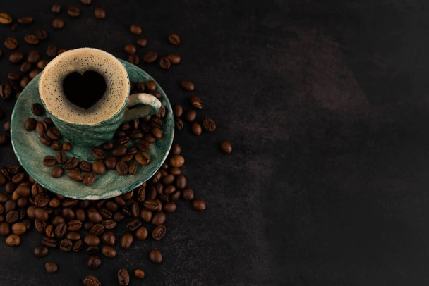Blurred image of a cup of coffee and scattered grains on a dark background with space for writing text.Coffee love concept. - Photo, Image