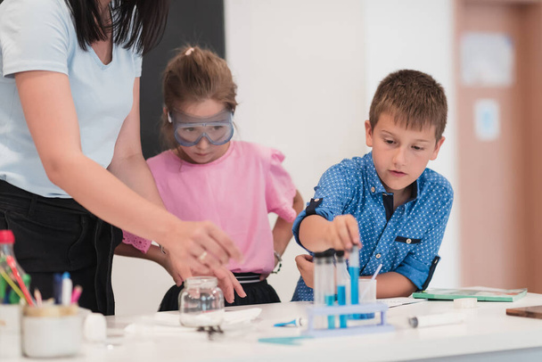 Elementary School Science Classroom: Enthusiastic Teacher Explains Chemistry to Diverse Group of Children, Little Boy Mixes Chemicals in Beakers. Children Learn with Interest. High quality photo - Fotó, kép