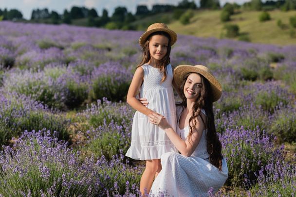 happy woman hugging daughter and looking at camera in lavender field - Fotó, kép