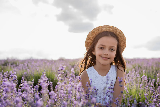 happy child in straw hat looking at camera in lavender field - Fotó, kép