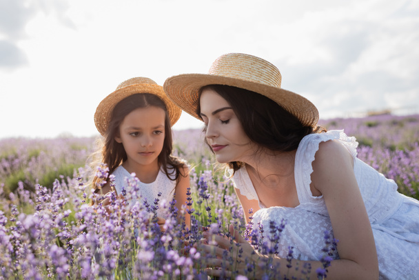 woman with closed eyes smelling aromatic lavender near daughter in field - Valokuva, kuva