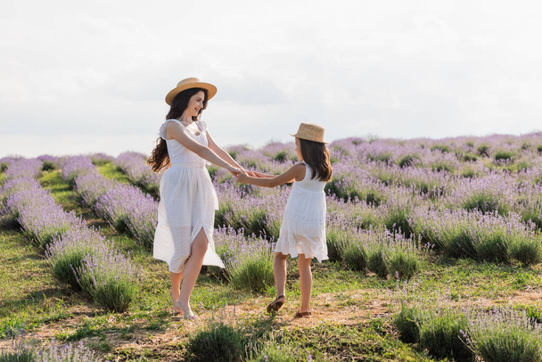 happy woman and girl in straw hats dancing in lavender meadow - Foto, imagen