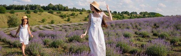 woman and child in white dresses and straw hats walking in blooming meadow, banner - Foto, imagen