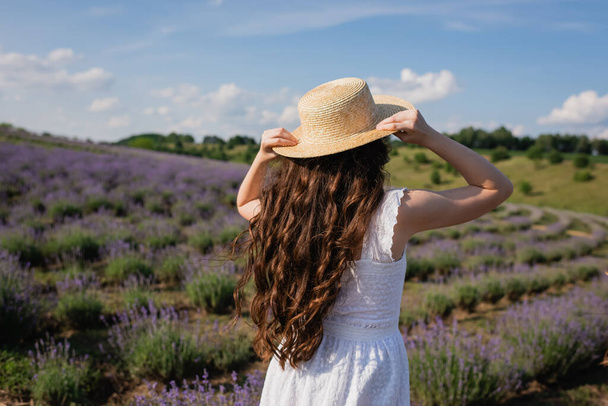 back view of child with long hair holding straw hat while standing in meadow - Foto, Imagem