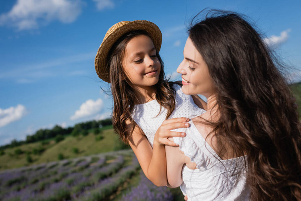brunette woman with long hair holding daughter in straw hat outdoors - Foto, Bild